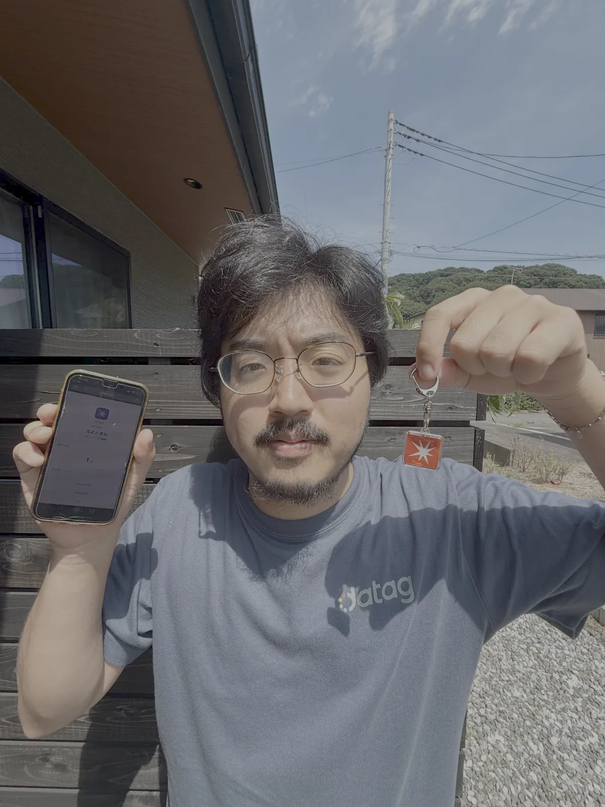 GeGeGe の会員が、片手に会員ページを開いたスマホ、もう片方にロゴ入り NFC キーホルダーを掲げているシーン